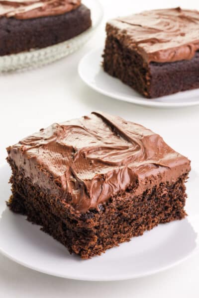 Delicious slices of whole wheat chocolate cake elegantly arranged on plates. The foreground features a prominent slice adorned with rich and glossy chocolate ganache frosting, promising a decadent and delightful plant-based dessert experience.