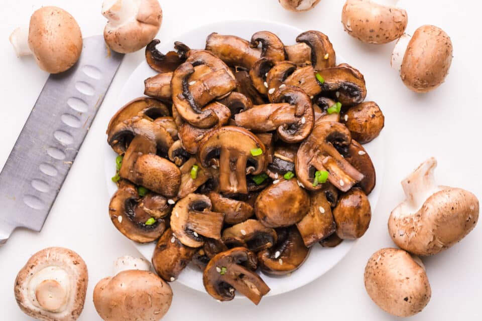 Looking down on sautéed mushrooms on a plate sitting next to whole mushrooms and a knife.