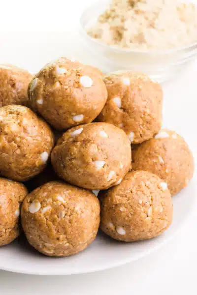 A stack of vanilla bliss balls sits in front of a bowl of vanilla protein powder.