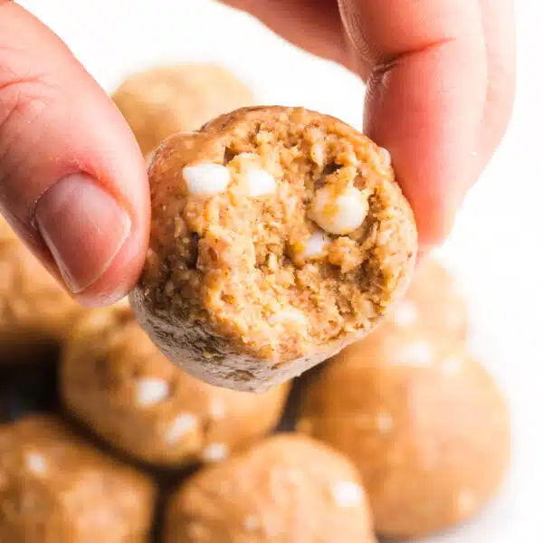 A hand holds a vanilla energy ball with a bite taken out, revealing white chocolate chips.
