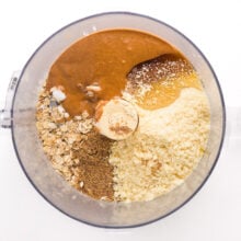 Looking down on ingredients in a food processor bowl, such as almond butter, oats, and more.