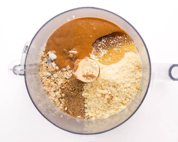 Looking down on ingredients in a food processor bowl, such as almond butter, oats, and more.