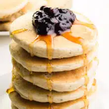 A stack of vegan bisquick pancakes has blueberries on top and drizzles of maple syrup.