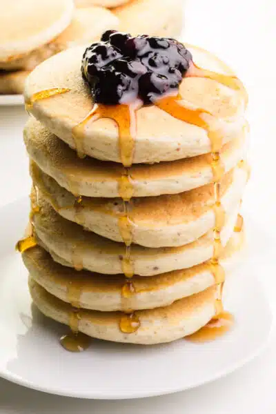 A stack of vegan Bisquick pancakes is topped with blueberries and has drizzles of maple syrup.