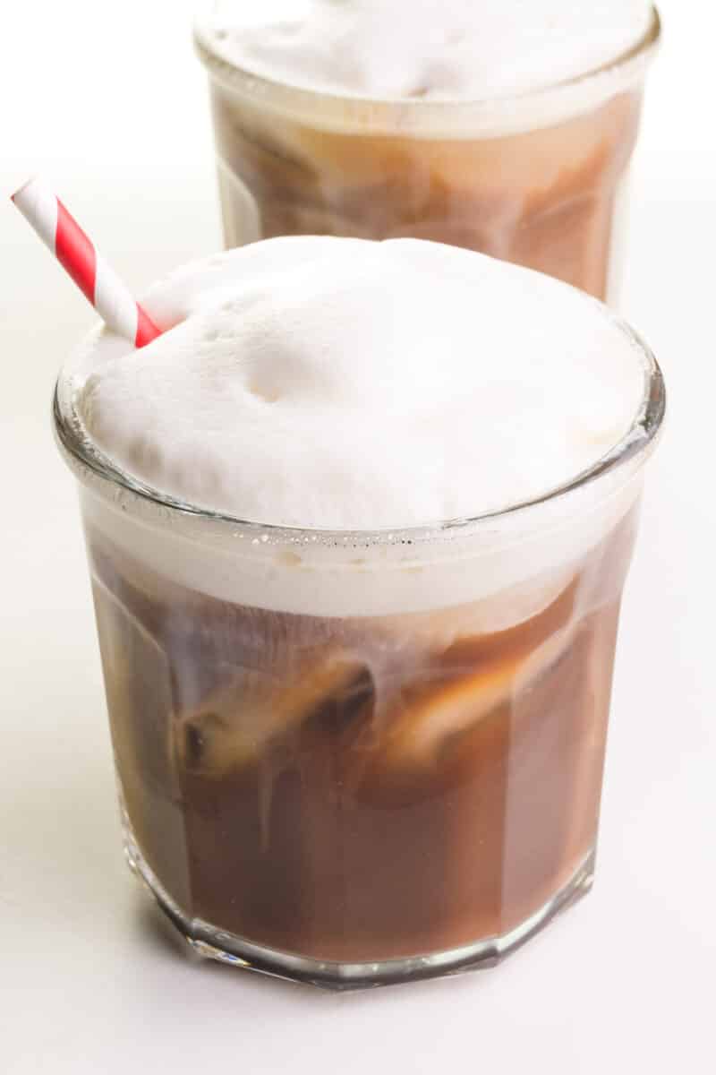 Two glasses of iced coffee is topped with vegan cold foam. The front glass has a red paper straw.