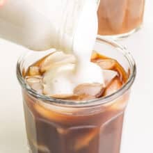 Vegan cold foam is being poured into an iced coffee drink.