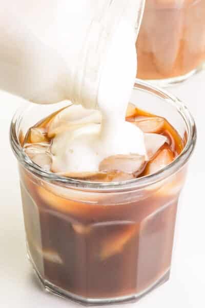 Vegan cold foam is being poured into an iced coffee drink.