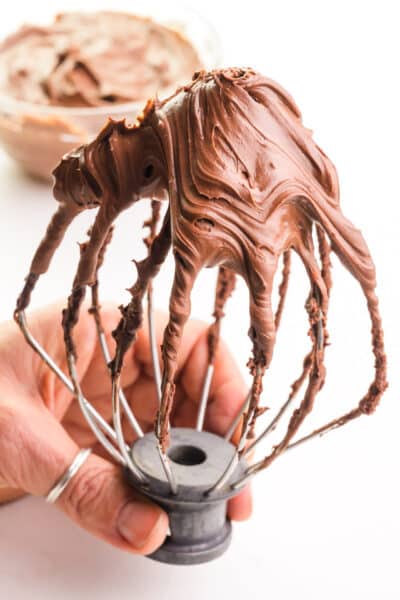 A stand mixer's whipping attachment is loaded with whipped chocolate ganache frosting.
