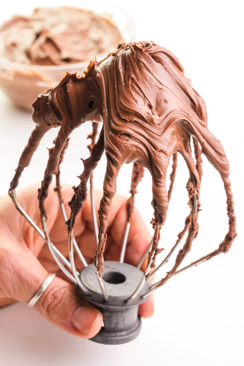 A stand mixer's whipping attachment is loaded with whipped chocolate ganache frosting.