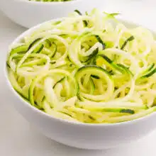 A bowl of fresh zucchini noodles on a white counter.