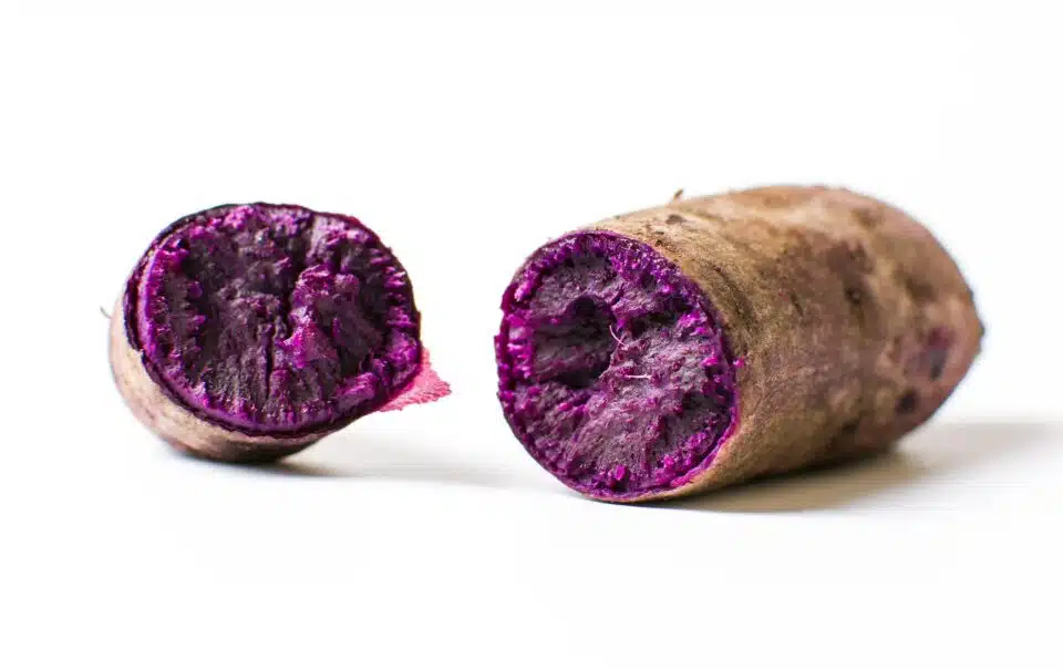 An ube purple yam is cut in half revealing vibrant purple flesh inside.