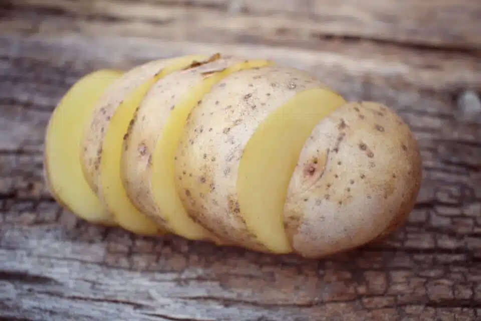 A raw potato cut into slices is on a wooden table.