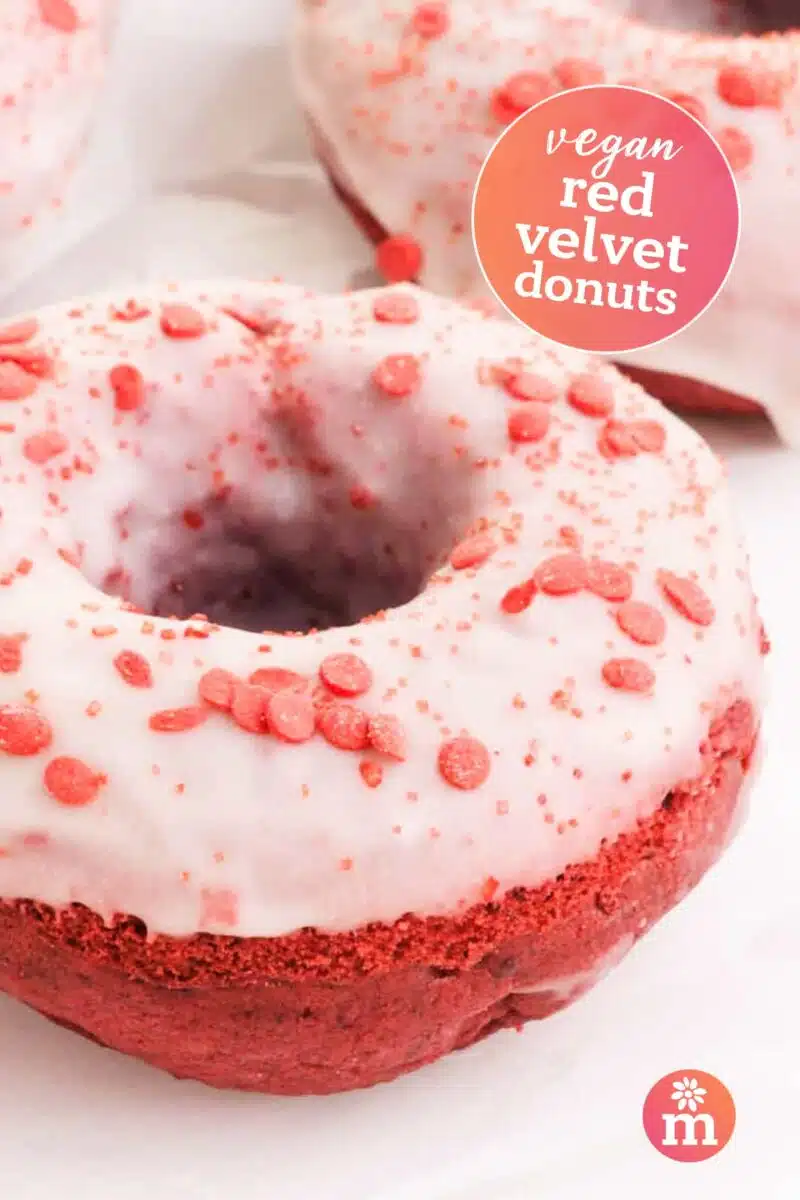 A closeup of a red donut with white glaze. The text reads, Vegan Red Velvet Donuts.