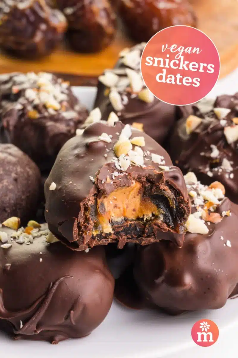 Date bites with peanut butter in the center and dipped in chocolate sit on a plate. Text reads, vegan snickers dates.