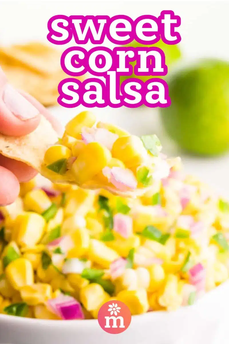 A hand holds a chip with corn on top hovering over a bowl with more of the dip. The text reads Sweet Corn Salsa.