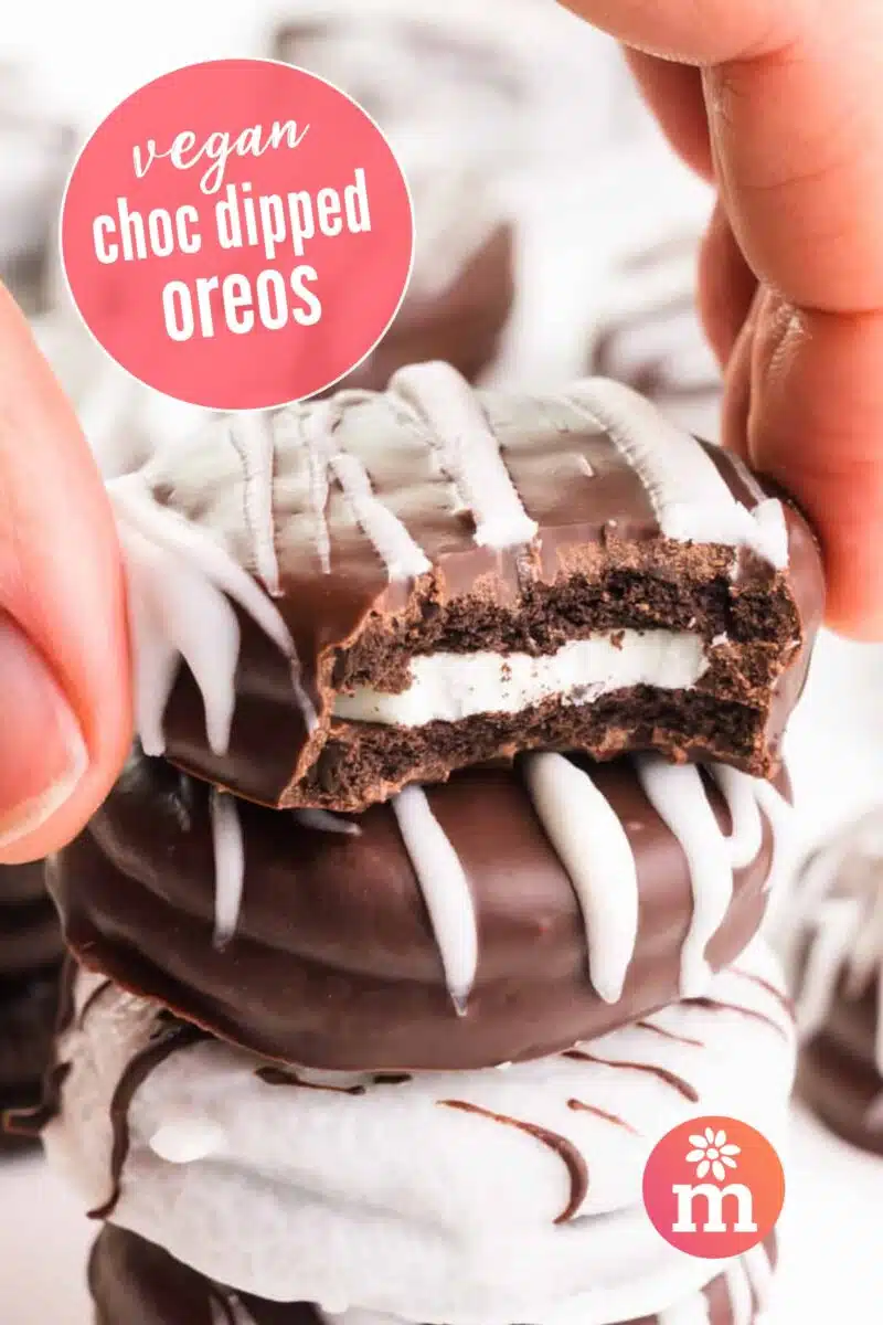 A hand grabs a cookie dipped in chocolate with a bite taken out. The text reads, vegan choc dipped Oreos.