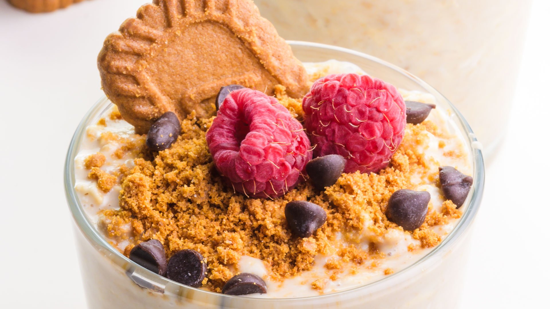 A bowl of Biscoff overnight oats has cookie crumbles, fresh raspberries, chocolate chips, and a Biscoff cookie on top.