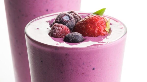 A closeup of a vibrant berry smoothie shows fresh and frozen fruit on top.