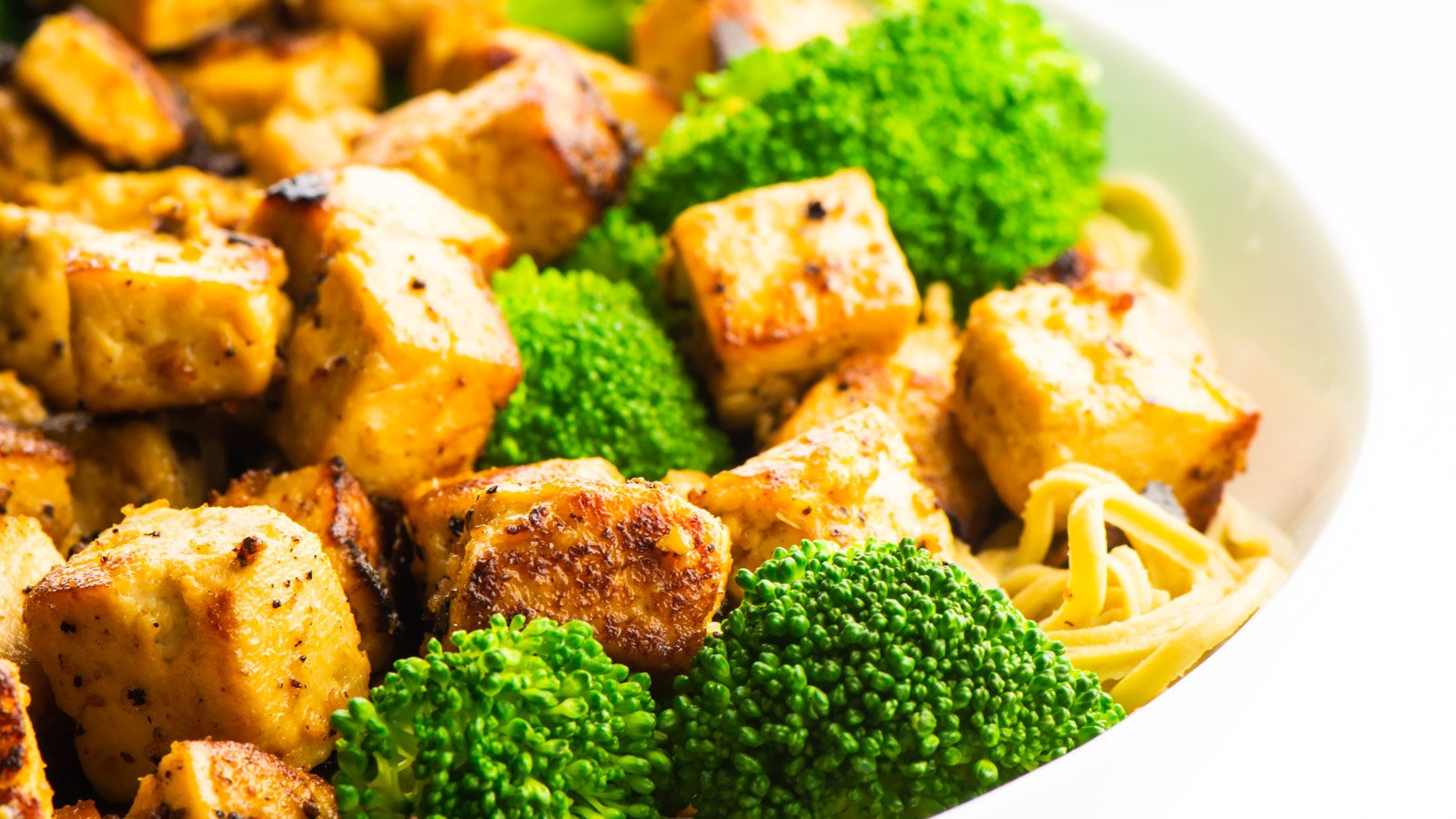 Miso tofu is cooked until golden brown around the edges. It sits in a bowl with broccoli and noodles.