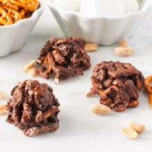 Chocolate-covered trail mix clusters surrounded by peanuts and ingredients in bowls