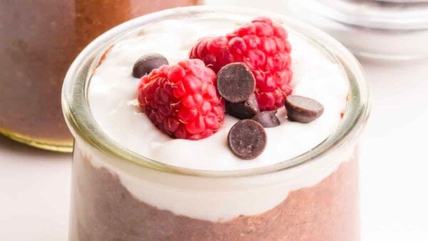 A closeup of chocolate flax pudding shows a yogurt topping and raspberries and chocolate chips on top.