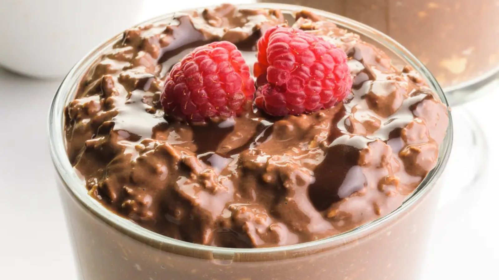 Vegan chocolate overnight oats are topped with chocolate sauce and fresh raspberries.