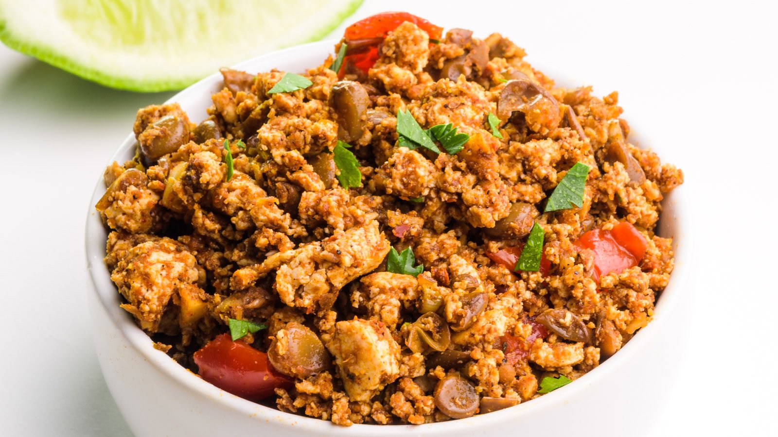 A bowl of tofu chorizo mix sits in front of a lime slice.