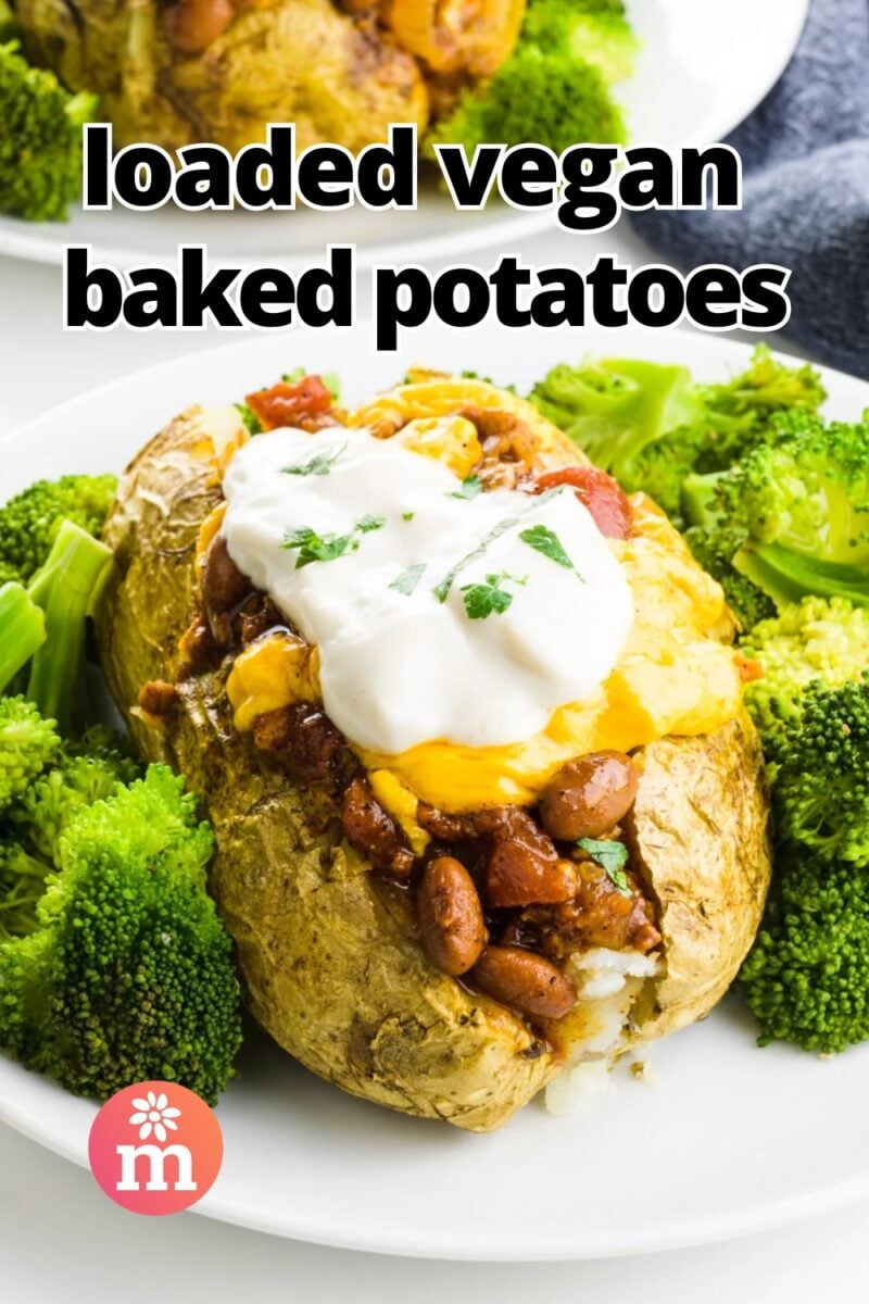 A baked potato topped wit chili, cheese and sour cream sits next to steamed broccoli on a plate. The text reads, Loaded Vegan Baked Potatoes.