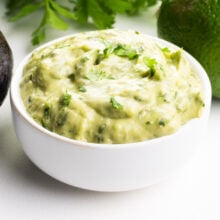 A bowl of cilantro lime avocado sauce sits on a white table.
