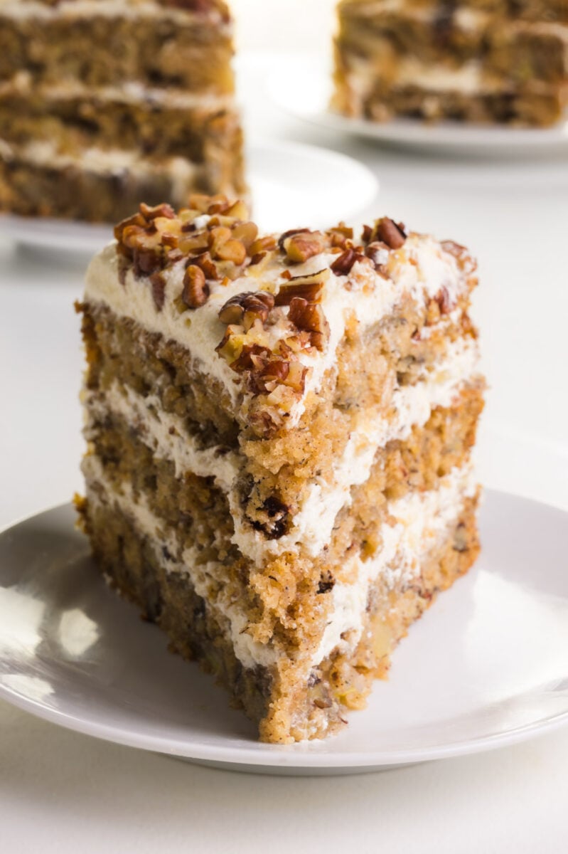 A slice of vegan hummingbird cake on a plate sits in front of two other slices in the background.