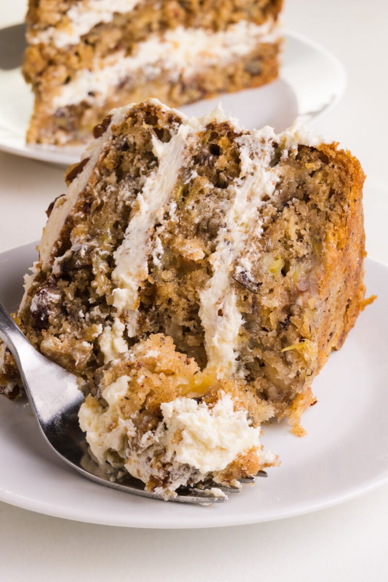 A slice of 3-layer cake is on its side on a plate and a biteful rests on a fork in front of it.