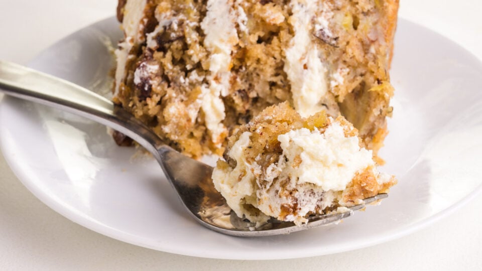 A slice of layered cake on its side has a forkful of cake sitting in front of it.