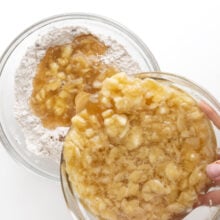 A bowl of liquid cake batter mixture is being poured into a bowl with dry ingredients, such as flour.