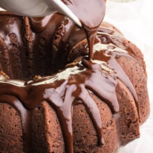 Chocolate sauce is being poured over a chocolate Bundt Cake.