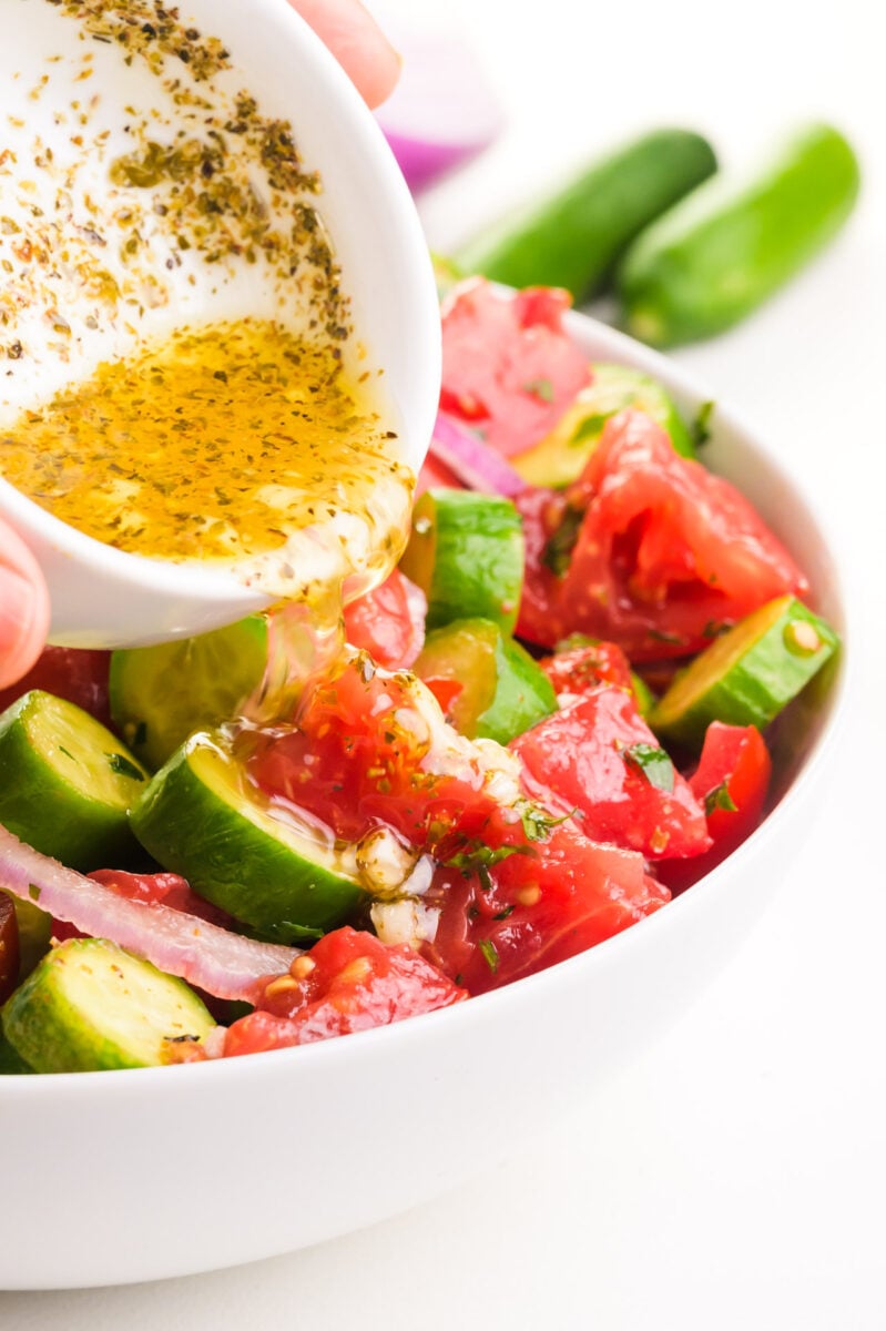 Dressing is being poured over a tomato cucumber salad.