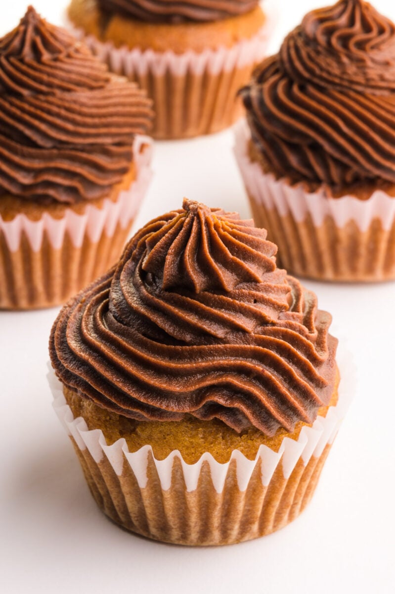 Several vanilla cupcakes are topped with swirls of chocolate frosting.
