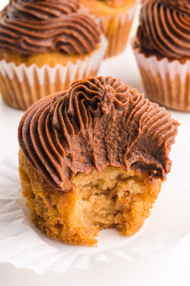 A yellow cupcake has chocolate swirls of frosting on top and a bite taken out.