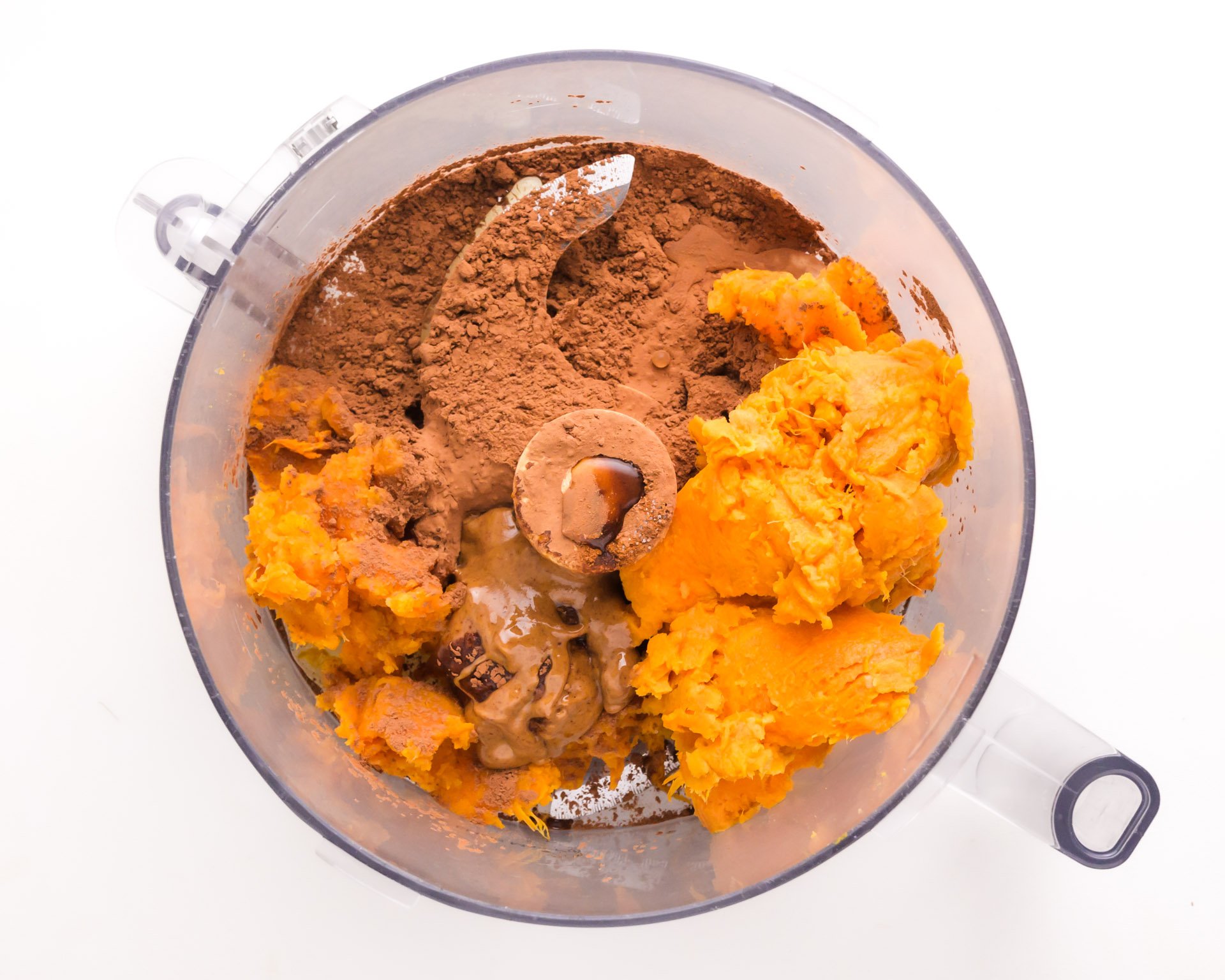 Looking down on a mixture in a food processor bowl, such as sweet potatoes, cocoa powder, and more.