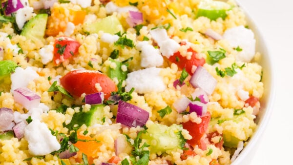 A closeup of a bowl of couscous salad with chopped tomatoes and other veggies.