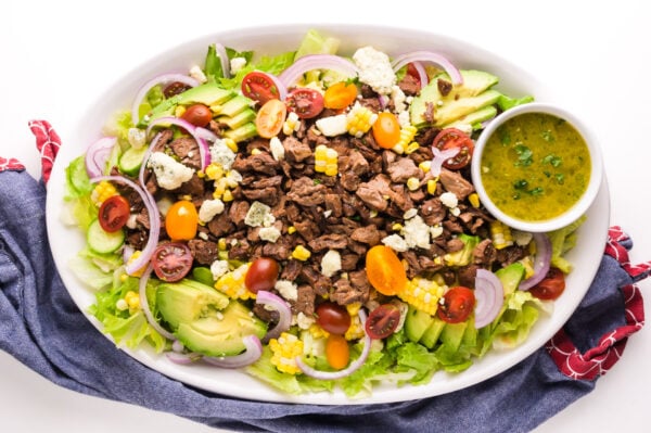 Looking down on a salad on a platter topped with vegan steak and veggies.