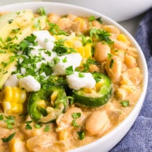 A bowl of white bean chili is topped with sour cream, sliced jalape&ntilde;os, and other veggies.