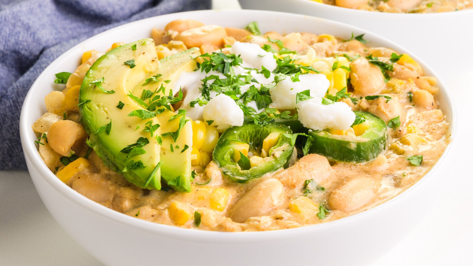 A bowl of white bean chili is topped with sour cream and veggies.