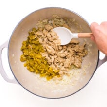 A hand stirs ingredients in a large pot.