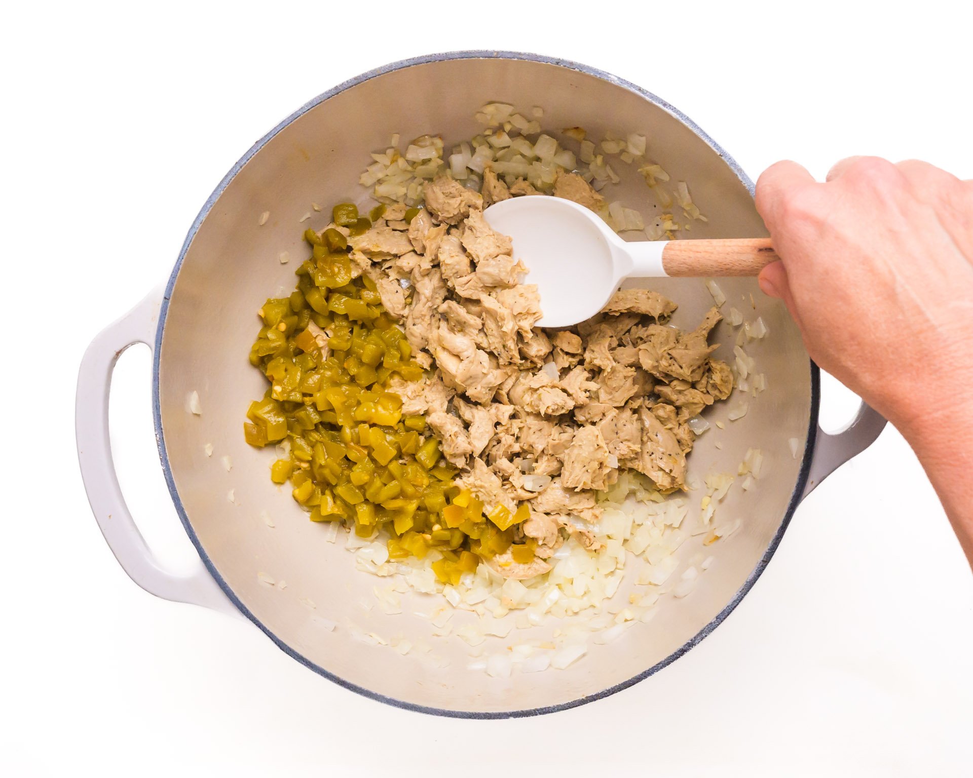 A hand stirs ingredients in a large pot.
