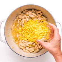 A hand pours corn into a pan with other ingredients.