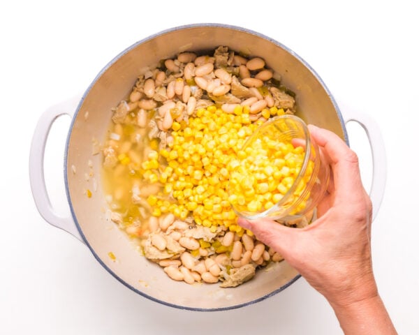 A hand pours corn into a pan with other ingredients.
