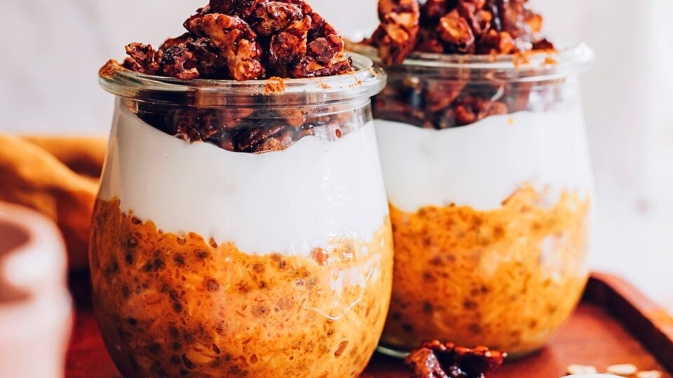 Two dishes of overnight oats have layer of pumpkin, yogurt, and a granola topping.