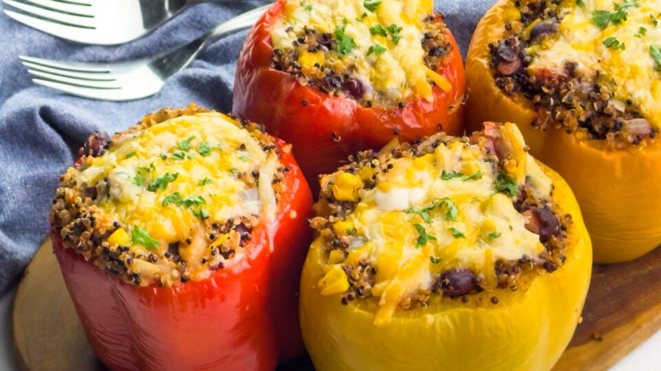 Several quinoa stuffed peppers are on a cutting board.