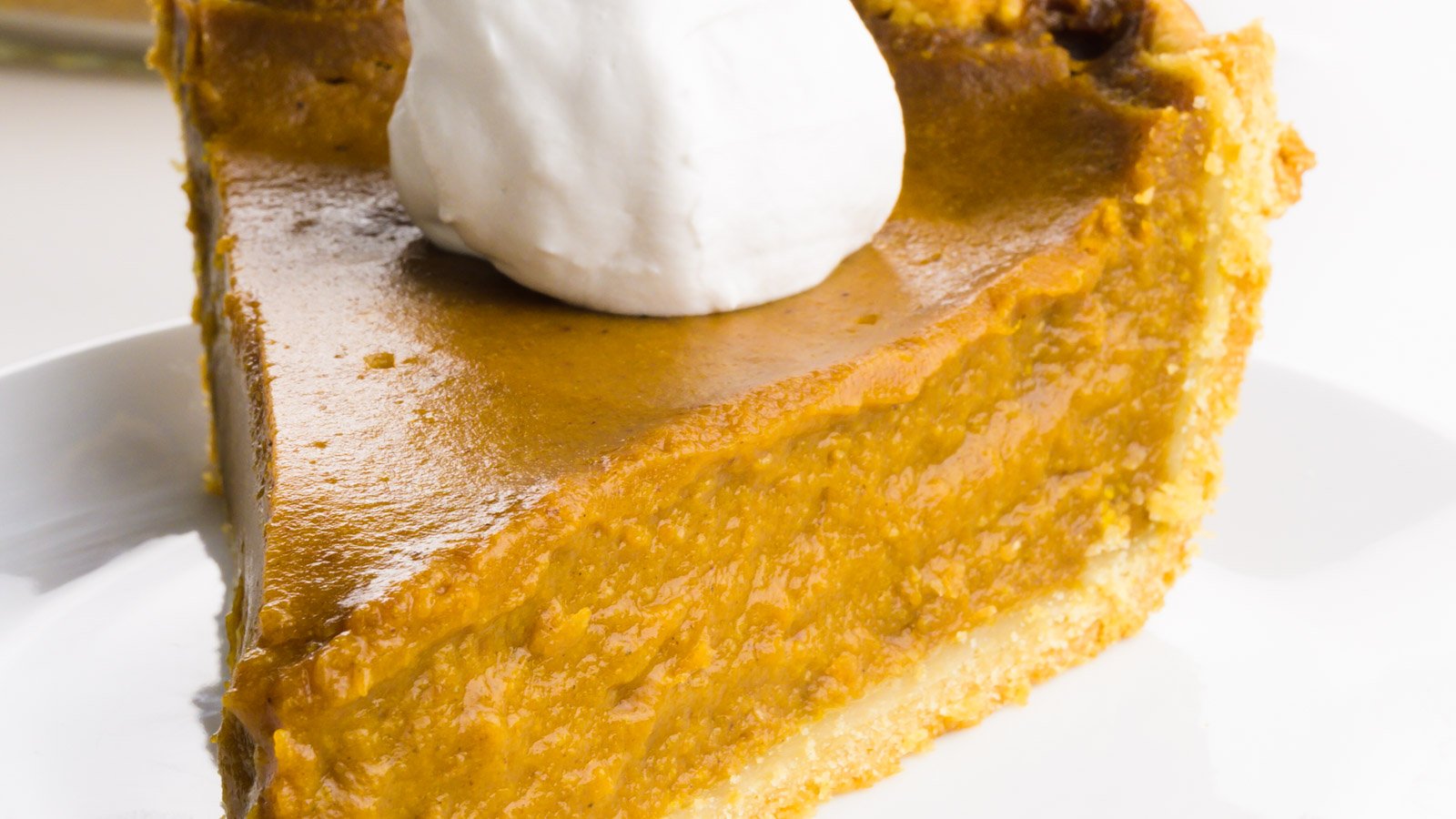A slice of pumpkin pie on a plate with whipped cream on top.