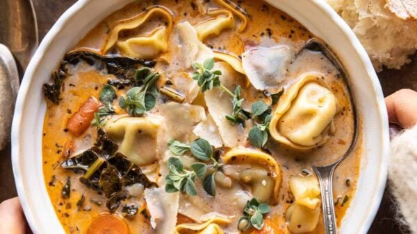 A bowl of tortellini soup has fresh herbs on top.
